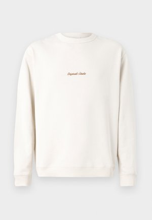 Krémová mikina s rebrovaným výstrihom a manžetami. Na hrudi má malé zlaté výšivky "Original Studio". Mäkka textúra.