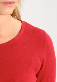 Pull en tricot rouge avec un col rond, texture douce et détails de couture délicats le long de la couture d'épaule. Sans motifs ni quincaillerie.