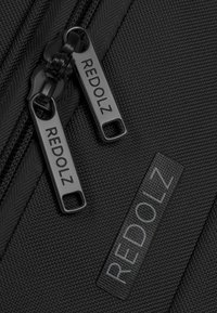 Tela negra texturizada con dos tiradores de zipper y una etiqueta, todos embellecidos con el nombre de marca "REDOLZ."