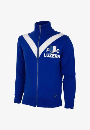 Blauwe trui met volledige ritssluiting, witte V-strepen, F C Luzern tekst, schildembleem op de borst, geribde boorden en hoge kraag.
