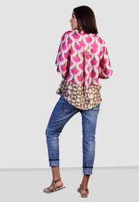 Langarmhemd mit rosa und braunen geometrischen Mustern, kombiniert mit hellblauen Jeans mit aufgerollten Säumen und beige Sandalen.