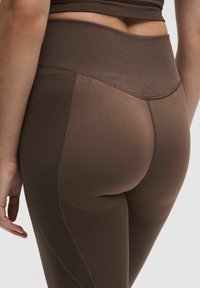 Leggings marron taille haute avec une ceinture côtelée, un panneau texturé à motifs et un tissu lisse, conçus pour le confort et la flexibilité.
