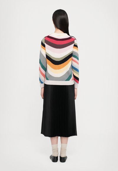 Maglione lavorato a maglia colorato con motivo a zig zag, che presenta tonalità di rosa, rosso, grigio e giallo. Abbinato a una gonna nera plissettata.