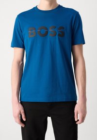 Camiseta de algodón azul de cuello redondo con un audaz logo negro de "BOSS" en la parte frontal, con mangas cortas y un ajuste estándar.
