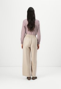 Světle pruhovaná, dlouhá rukávová košile v barvě mauve, spárovaná s béžovými kalhotami s širokými nohavicemi a elastickým pasem. Elegantní obuv s potiskem zvířecí kožešiny.