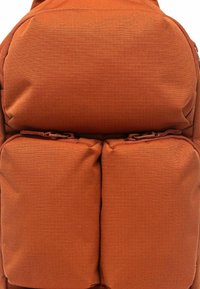 Zaino in tessuto arancione con forma rettangolare, due tasche frontali con cerniere e superficie testurizzata per una presa migliore.