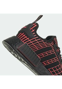 Černá sportovní obuv s mřížkovým vzorem v červené barvě, texturovanou podrážkou, poutkem a polstrovanou mezipodešví. Zaoblená špička a design na šněrování.