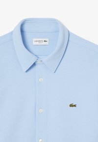 Polo shirt slim fit di colore blu chiaro con tessuto testurizzato, dotato di colletto a due bottoni e piccolo logo di coccodrillo ricamato in verde.