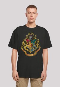 Black cotton t-shirt featuring a colorful Hogwarts crest design with a gold border, displaying various mythical creatures and text.