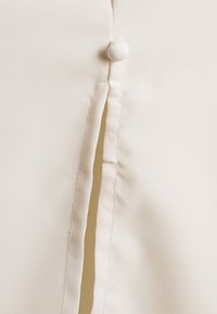 Světle béžová tkanina s knoflíkovým zapínáním a bočním rozparkem. Hladká textura podtrhuje minimalistický design a čisté linie.