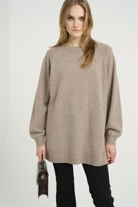 Beige kötött pulóver hosszú raglán ujjal és bordázott aljjal. Sötét nadrággal viseli, amelyet egy kis barna táskával tart.