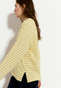 Maglietta a maniche lunghe a righe gialle con una vestibilità comoda, caratterizzata da sottili righe marroni e fessure laterali all'orlo, realizzata in tessuto morbido.