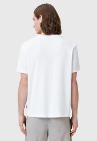 T-shirt bianco in cotone con una vestibilità rilassata, maniche corte e collo tondo. Il retro presenta un design minimalista senza loghi o motivi.