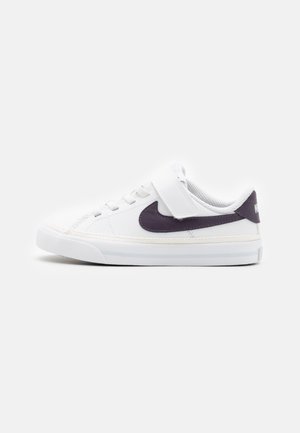 Biały niski sneaker z czarnym logo Nike, sznurówkami i paskiem na rzep na jednolitym jasnym tle, widok z boku na lewo.