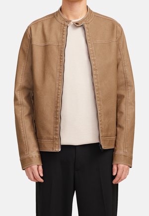 Hombre vistiendo una chaqueta de cuero marrón con cremallera sobre un suéter de canalé crema y pantalones negros, mostrado desde el cuello hasta la cadera contra un fondo liso.