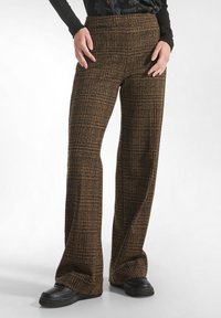 Brown plaid wide-leg pants with a textured fabric and high waistband, paired with black shoes. Front view, hands on hips.