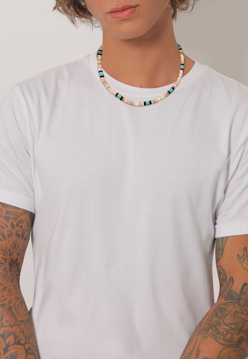 Hvid crew-neck t-shirt båret med en flerfarvet perlekæde, der har beige, blå og sorte perler, hvilket fremhæver en glat tekstur.