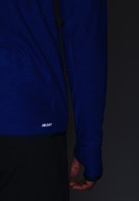 Långärmad sporttröja i djupblått med en texturerad yta. Har tumhål i ärmsluten och en liten "DRY"-logotyp vid fållen.