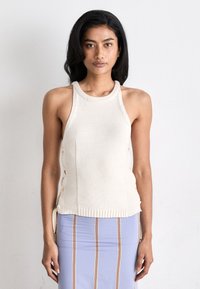 Λευκή πλεκτή τραχηλική μπλούζα με πλευρικές ανοίγματα, ραβδωτή υφή και εφαρμοστή γραμμή. Φορεμένη με μια ανοιχτό μπλε φούστα με κατακόρυφες ρίγες.