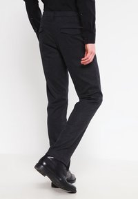 Mörkgrå skräddarsydda byxor i en texturerad tygkvalitet, med slim fit, slät front och två bakfickor. Bärs med svarta skor.