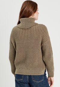 Chunky strikket sweater i dæmpet olivengrøn, med høj krave og ribbet tekstur. Vide ærmer og bundfarve med en afslappet pasform.