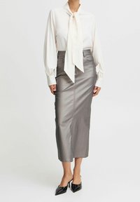 Blusa bianca con collo legato, maniche lunghe a sbuffo, abbinata a una gonna midi metallica argento e décolletée nere a punta.