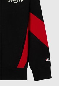 Manica di felpa nera con striscia diagonale rossa, tasca frontale, testo "19C19" sul petto e piccolo logo Champion vicino al polsino.