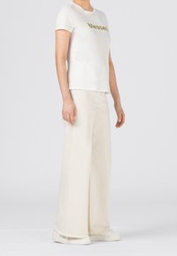 Vit bomull t-shirt med "blessed" i guldskrift, ihop med krämfärgade vida byxor och vita sneakers. Enkelt och avslappnat outfit.