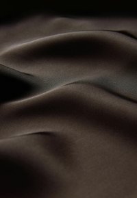 Glat, mørkebrun stof med bløde folder og subtil glans, der fremhæver teksturen og faldet.