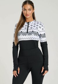 Maglia sportiva a maniche lunghe bianca e nera, con colletto a zip, motivo a fiocco di neve, e leggings neri aderenti con vita alta.