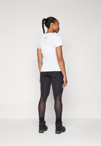 Hvit kortermet treningstopp med rund hals, sammen med svarte leggings med meshpaneler og svarte sporty sko.