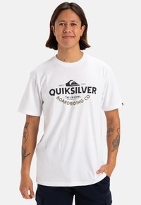 Camiseta de algodón blanca con un logotipo negro de Quiksilver y elementos de diseño. Mangas cortas y estilo de cuello redondo. Textura suave, ajuste casual.