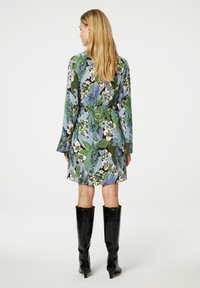 Blumenkleid mit langen Ärmeln in grün, blau und cremefarbigen Mustern. Kombiniert mit schwarzen, strukturierten kniehohen Stiefeln.