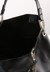 Black leather handbag with gold chain accents and a smooth texture. Features a spacious interior and a snap closure at the top.