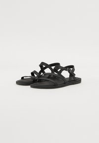Sandalias planas negras con múltiples tiras cruzadas, cierre de hebilla y un acabado suave y mate. Ligeras y con un diseño simple.