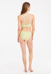 Zelené květinové bikiny s designem křížového zadního dílu, zdobené jemnými bílými květinovými vzory jak na horní, tak na spodní části.