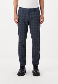 Pantalones de cuadros azul oscuro con corte slim, cintura media y una textura suave, acompañados de zapatos de cuero negros.