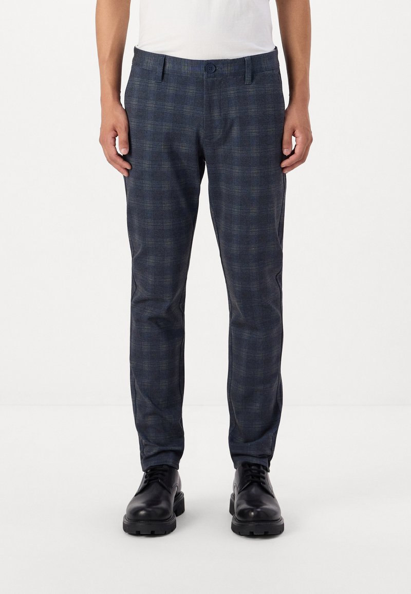 Pantalones de cuadros azul oscuro con corte slim, cintura media y una textura suave, acompañados de zapatos de cuero negros.