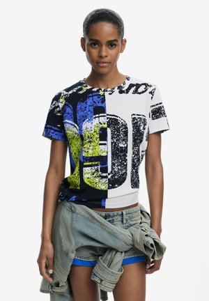 Graphic t-shirt featuring a color block design in navy, white, and neon yellow, with bold printed text and worn texture. Paired with denim shorts.