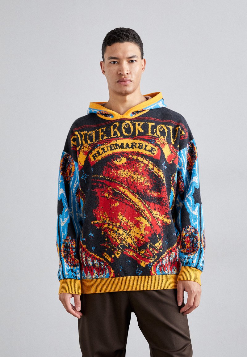 Sweater with an external knit pattern featuring vibrant colors including red, blue, and black. It has a yellow hood and ribbed cuffs.