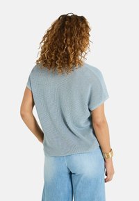 Top de punto azul claro de manga corta con un corte holgado, que presenta una superficie texturizada y un dobladillo recto, combinado con pantalones de mezclilla claros.