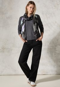 Maglione grigio con finitura testurizzata, pantaloni larghi neri e una sciarpa fantasia con forme geometriche e colori tenui. Sneakers casual.