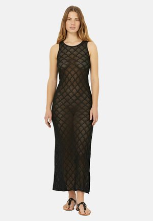 Schwarzes, ärmelloses, gestricktes Maxikleid mit einem Rautenmuster, ausgestattet mit einem Rundhalsausschnitt und seitlichen Schlitzen, kombiniert mit flachen Sandalen.