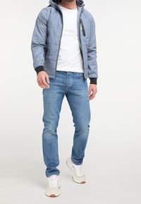 Lekka szara kurtka z zamkiem błyskawicznym na piersi, czarnymi mankietami i kapturem. Nosi się ją na białej koszuli i niebieskich dżinsach, dopełnioną białymi trampkami.