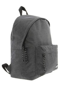 Mochila de tela gris con forma redondeada, correas ajustables negras, bolsillo frontal y acentos de cordón en blanco y negro.