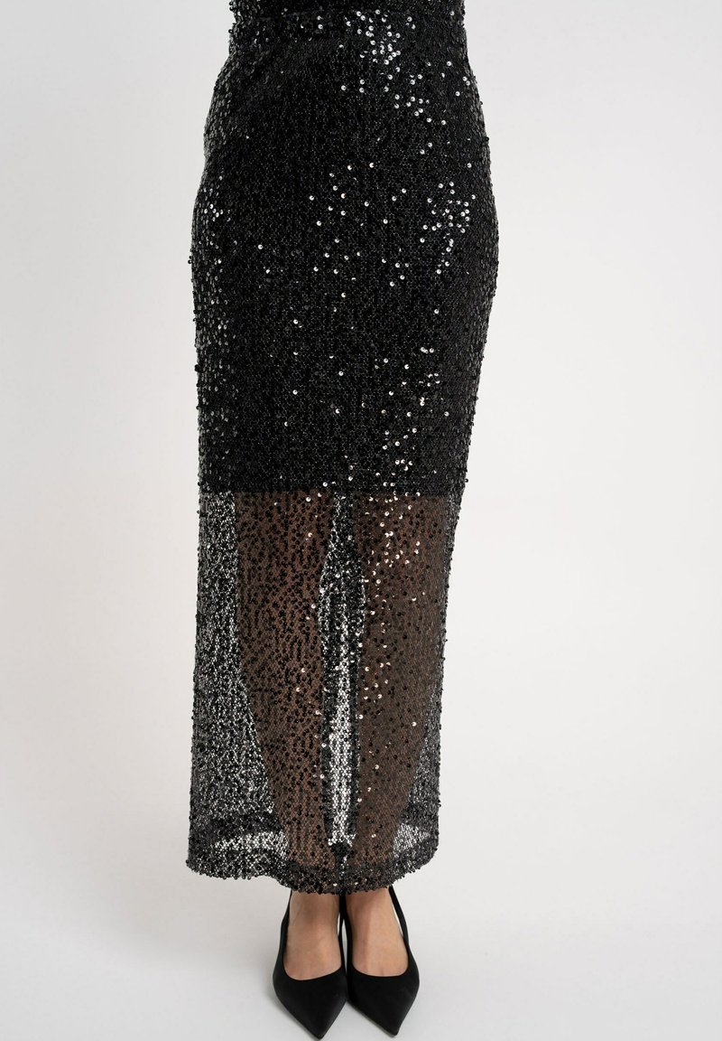 Czarna spódnica z cekinami z przezroczystą dolną częścią. Posiada dopasowany krój i długość do połowy łydki, zestawiona z czarnymi szpilkami w szpic.