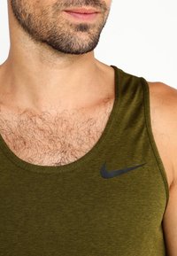 Débardeur Nike vert olive avec un col arrondi et un petit logo noir sur la gauche. Texture douce et design sans manches.