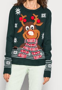 Pull tricot vert avec un motif de renne, des accents rouges, des pompons et des motifs de flocons de neige. Poignets côtelés avec des détails blancs.