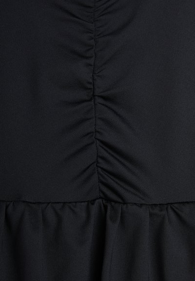 Svart stoff med rynket og samlet sømdetalj som går vertikalt og en samlet rysjekant nederst.