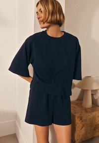 Marinblå ribbad trikå lounge-set bestående av en löst sittande t-shirt med kort ärm och matchande shorts. Enkel, ren design utan synliga detaljer.